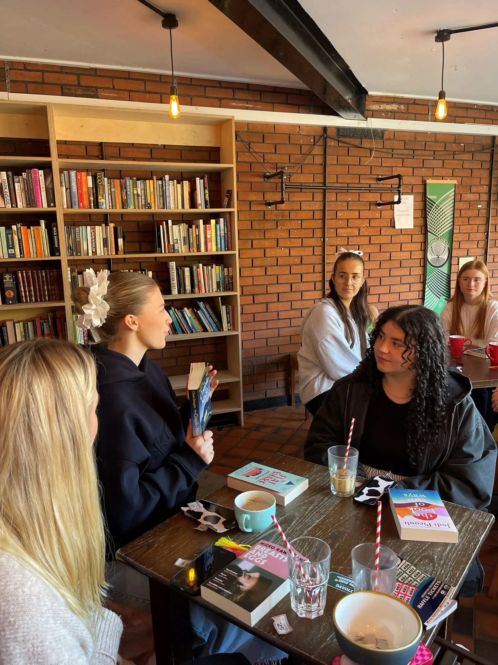 A woman holding up a book as others look on round a café table, with shelves of books behind