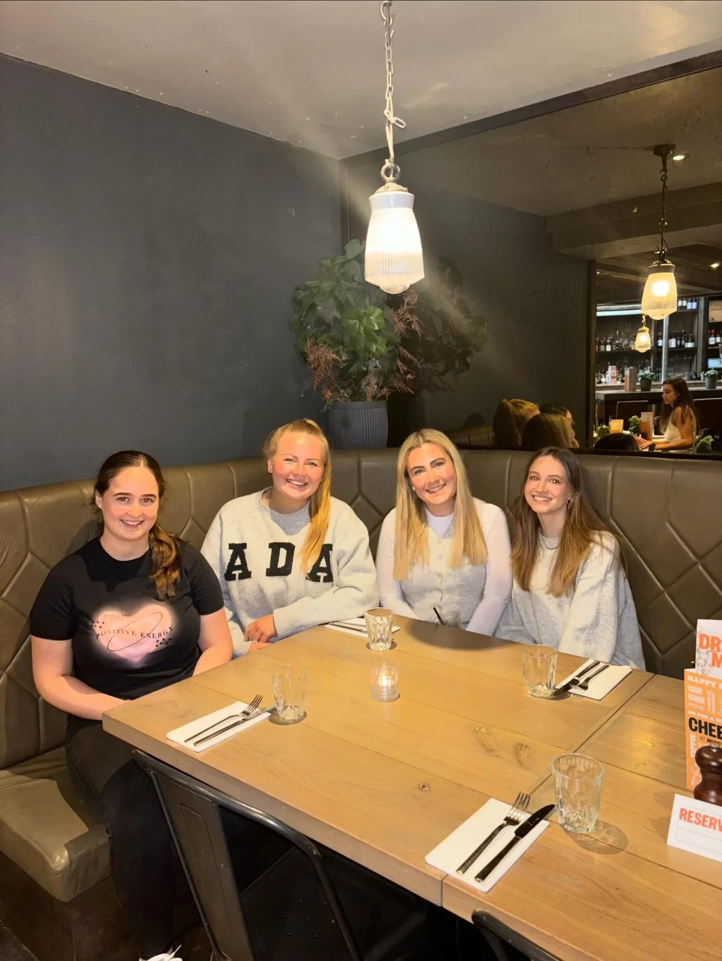 Four women smiling side by side in a leather booth at a restaurant table set with cutlery