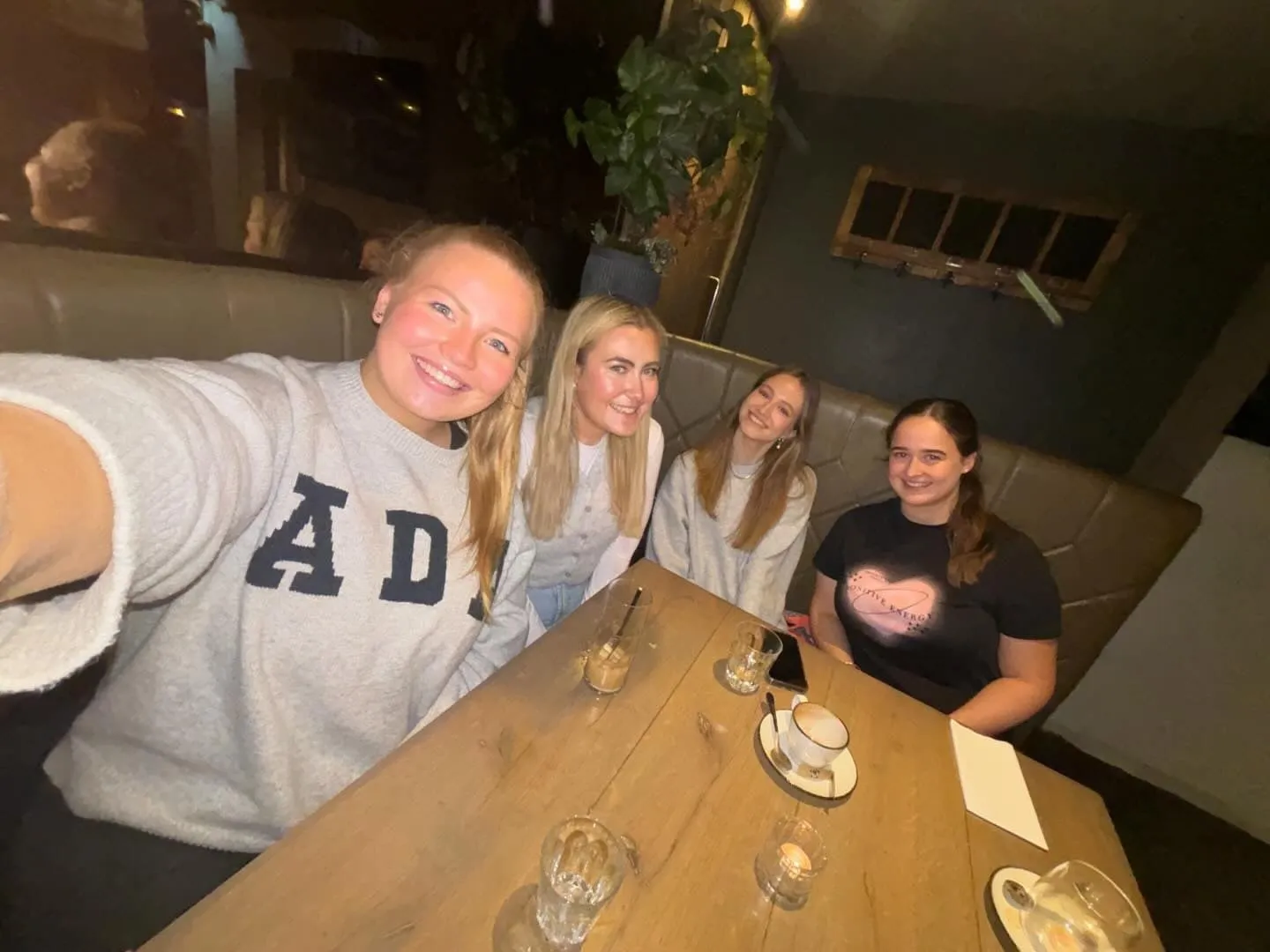 A selfie of four women in a leather booth, with drinks and a tea light on the table