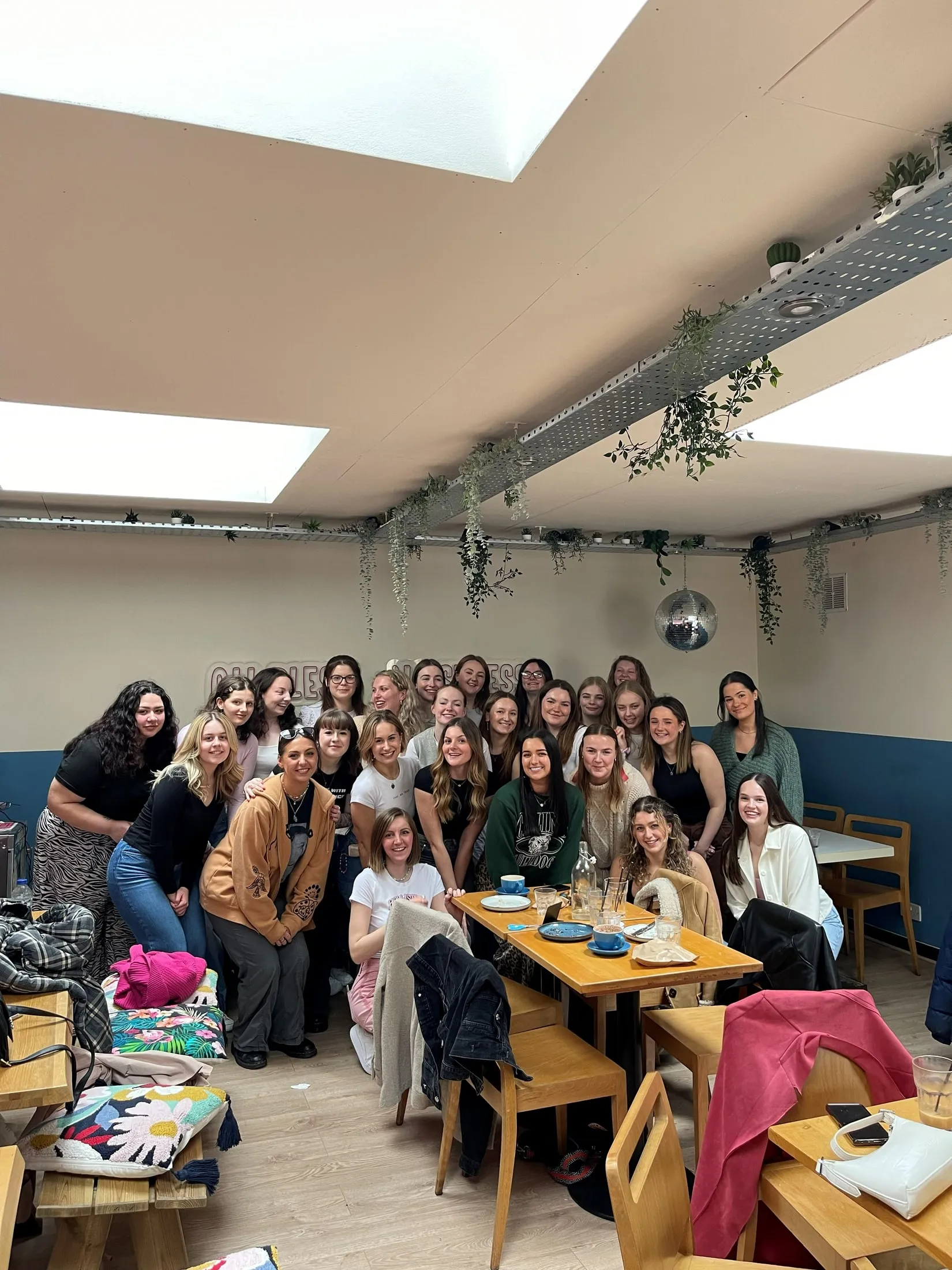 A big group of women posing together under trailing plants and a disco ball