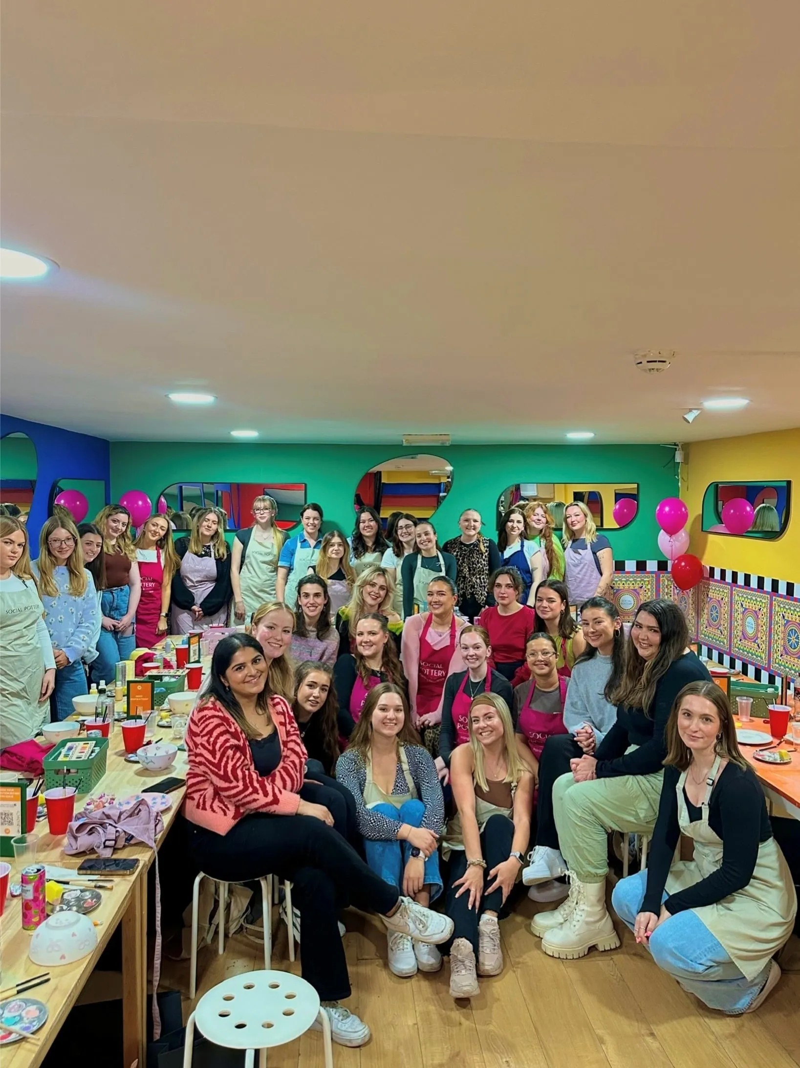A big group at a pottery painting night in a bright green and pink room