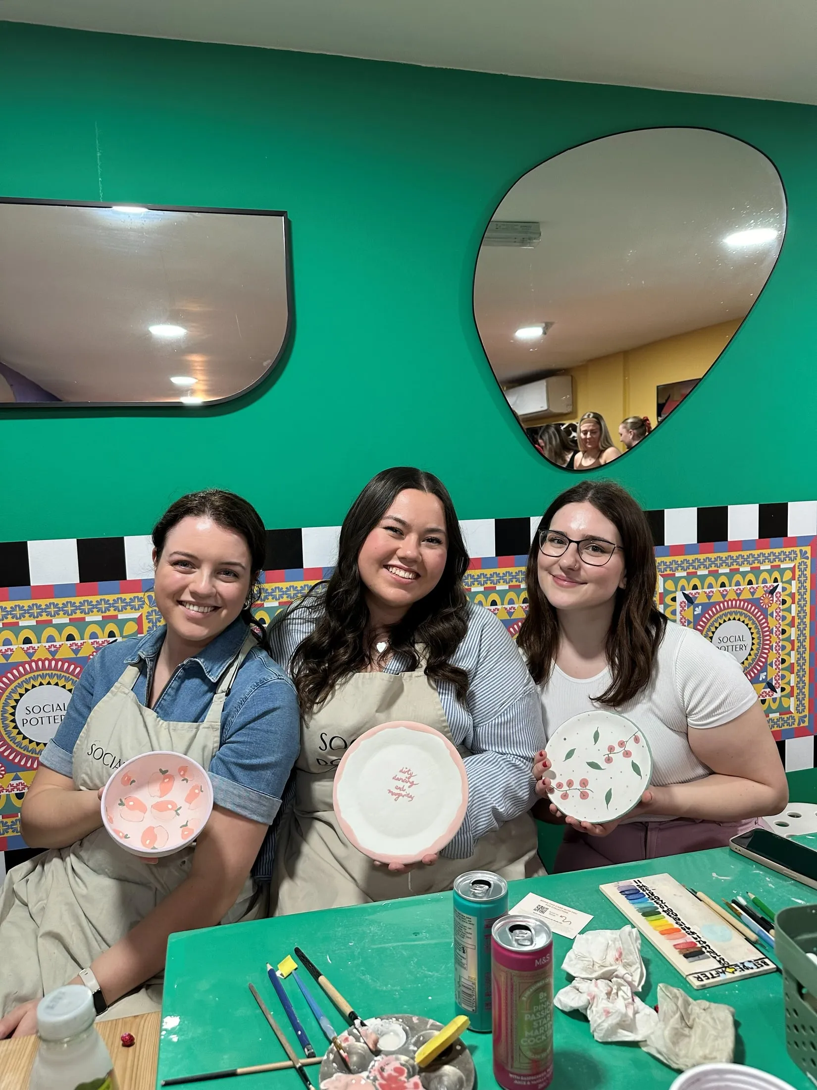 Three women holding up the plates they painted