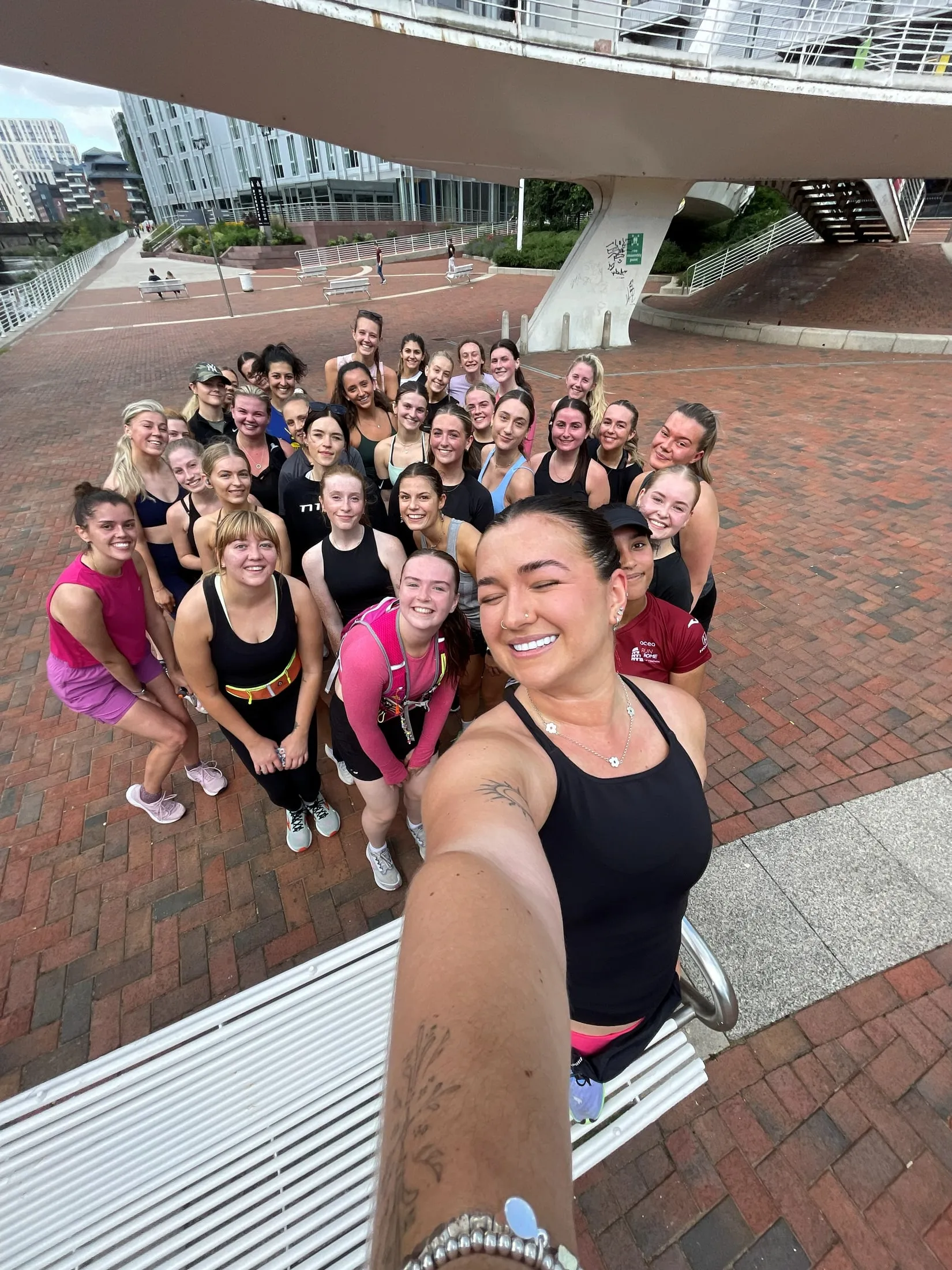 A big group of women in sportswear in a selfie on a paved square