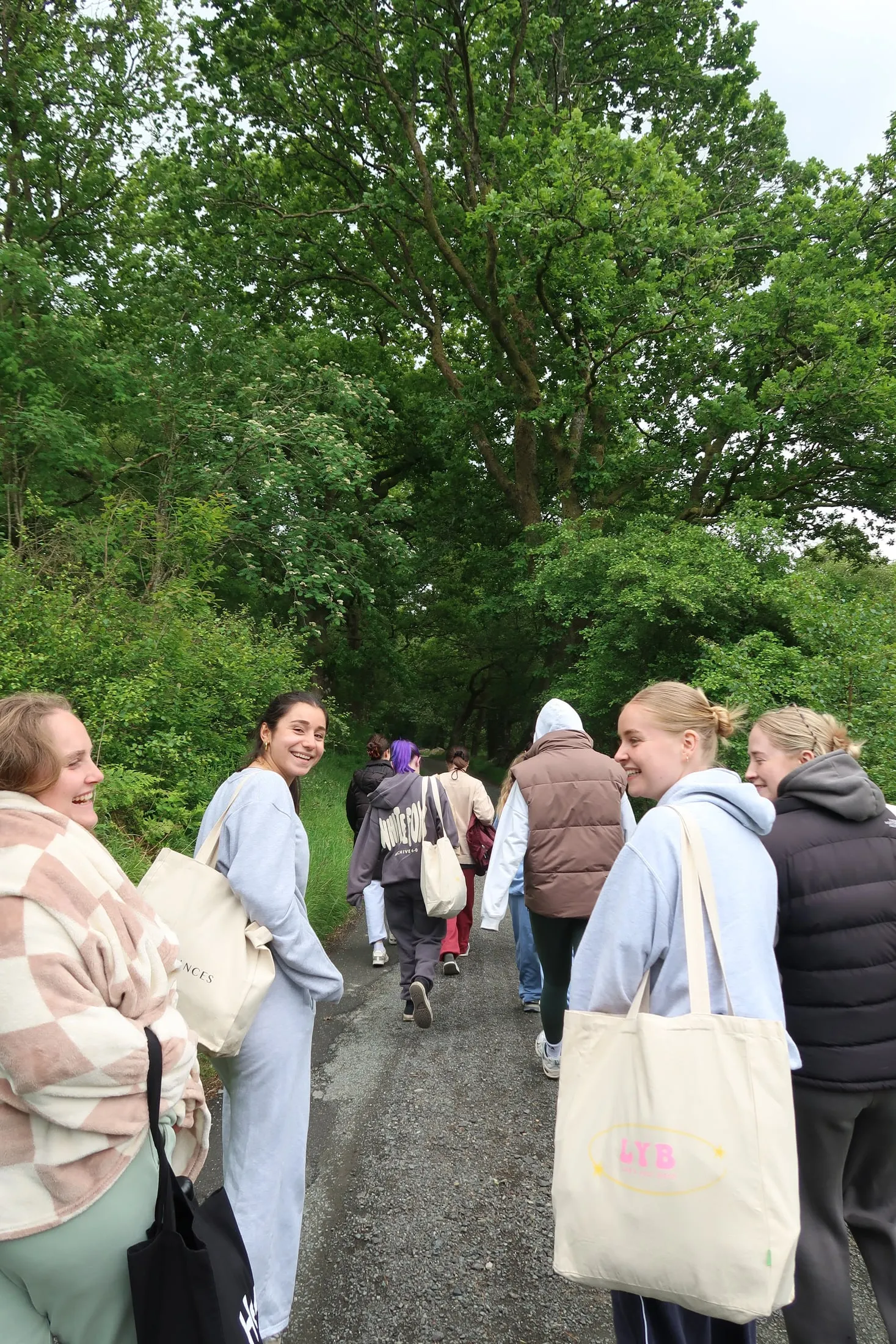 A group walking along a woodland path, one carrying an LYB tote bag