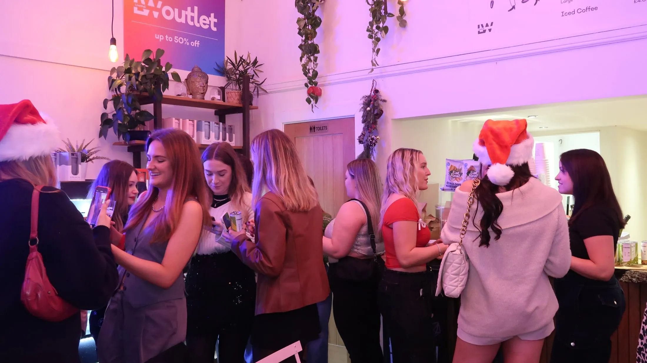 Women chatting by a café counter in pink and purple light, two of them in Santa hats