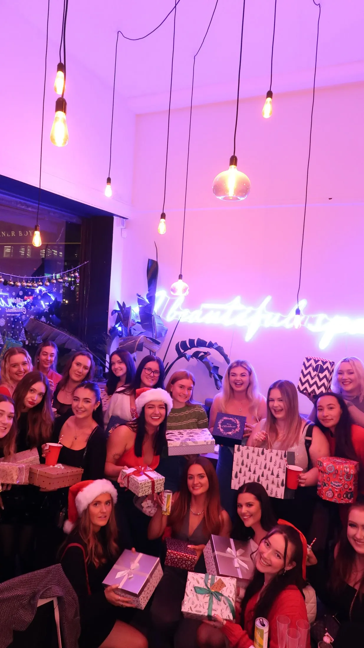 A Christmas party under pink neon lights, everyone holding presents