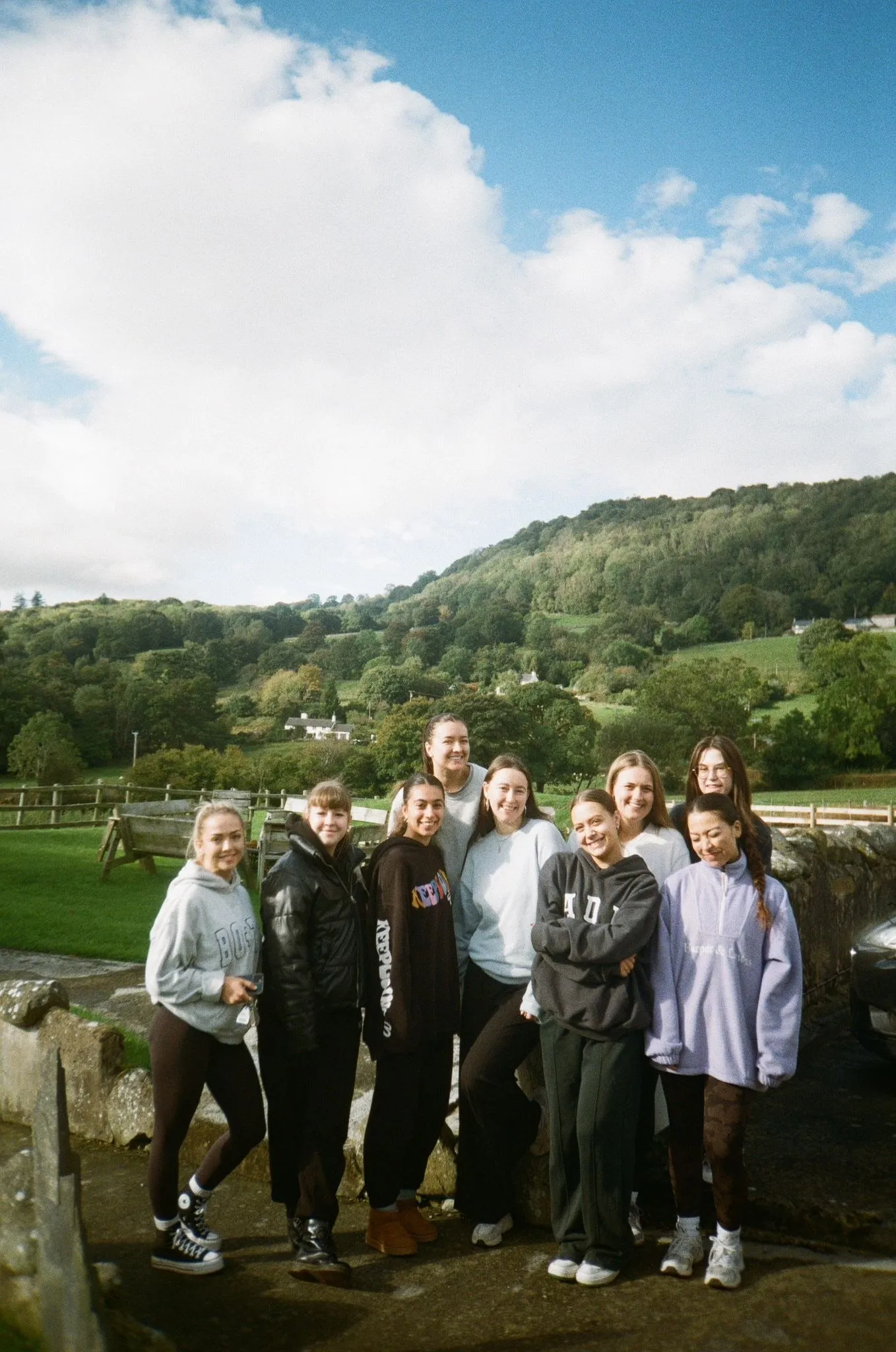 A group of women posing together on a path in green hills, shot on film