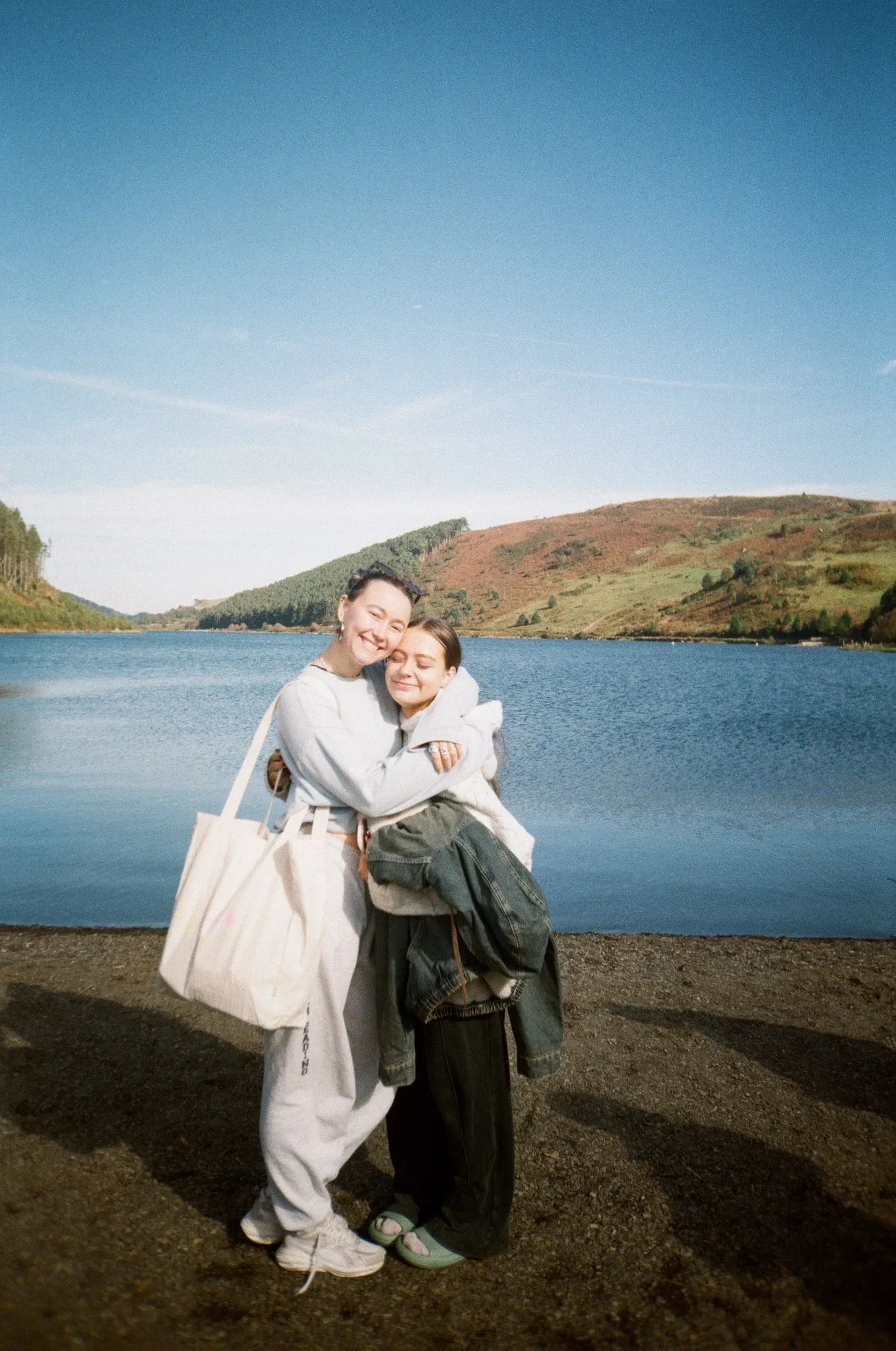 Two women hugging and laughing on a lakeshore, shot on film