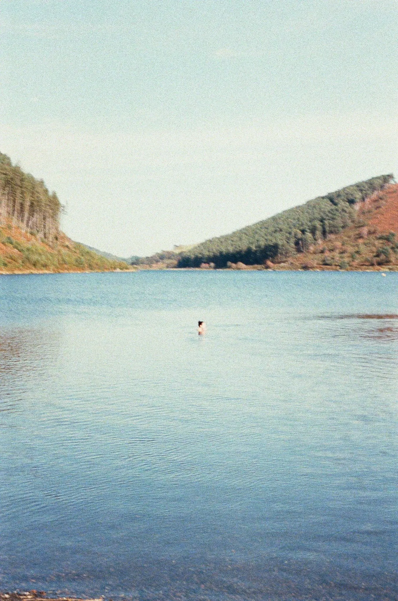 A lone swimmer far out on a still lake between the hills, shot on film