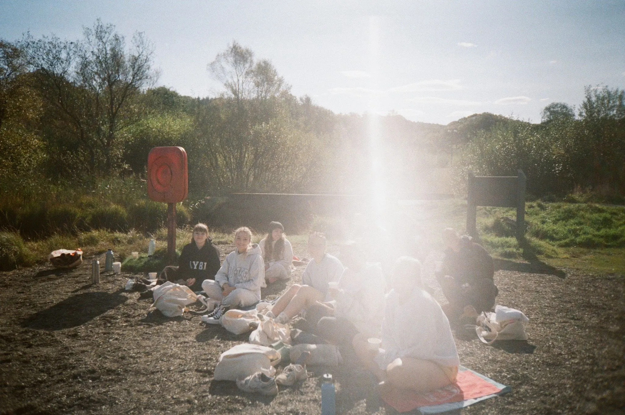 A group sitting on a lakeshore in bright sun, with a flare of light, shot on film