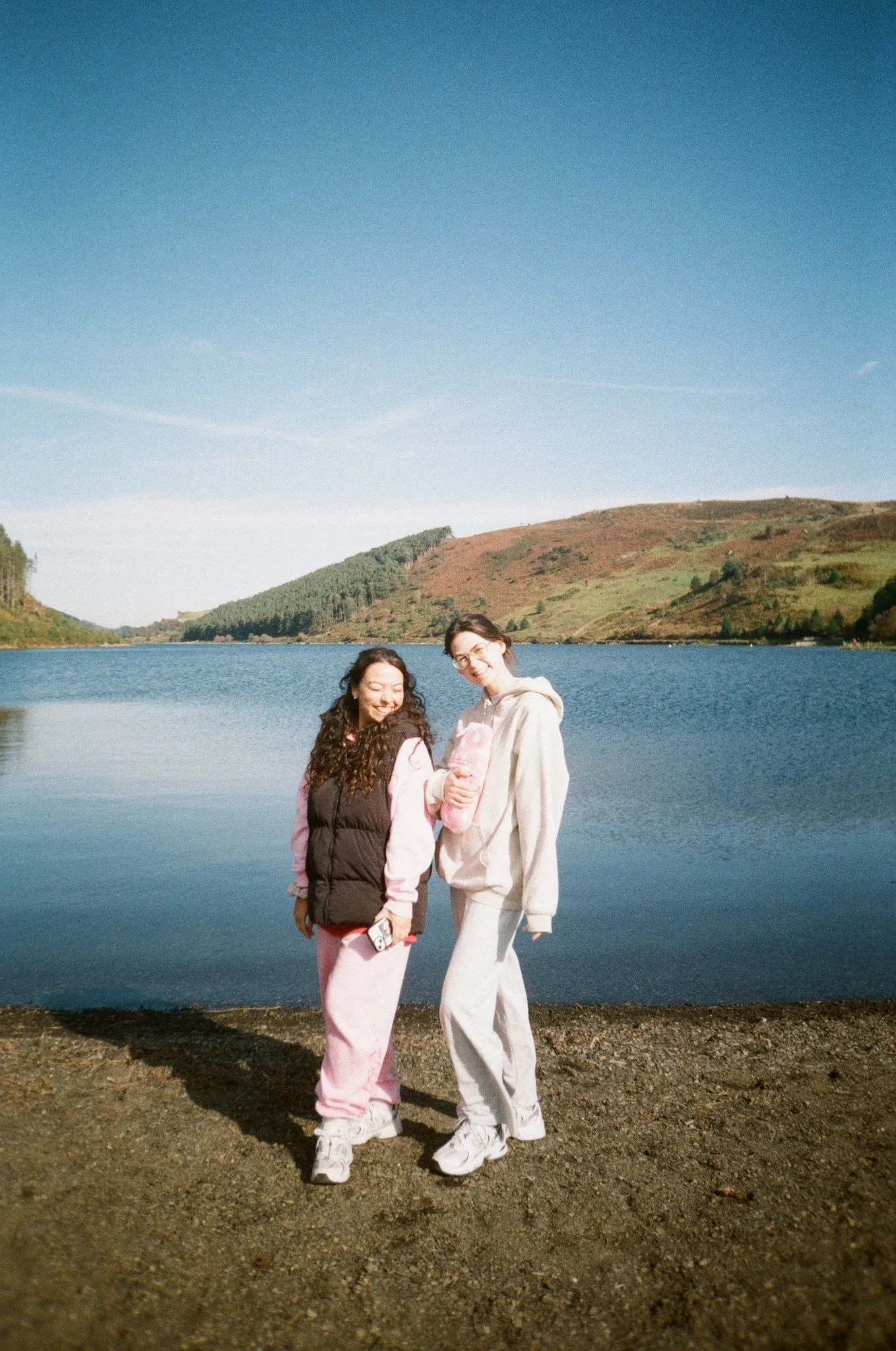 Two friends on a lakeshore, one in pink joggers, shot on film
