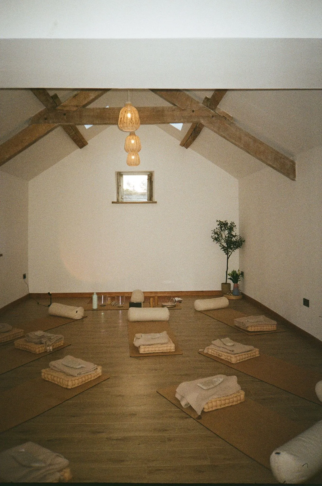 An empty studio under wooden beams, blankets folded on floor cushions and mats, shot on film