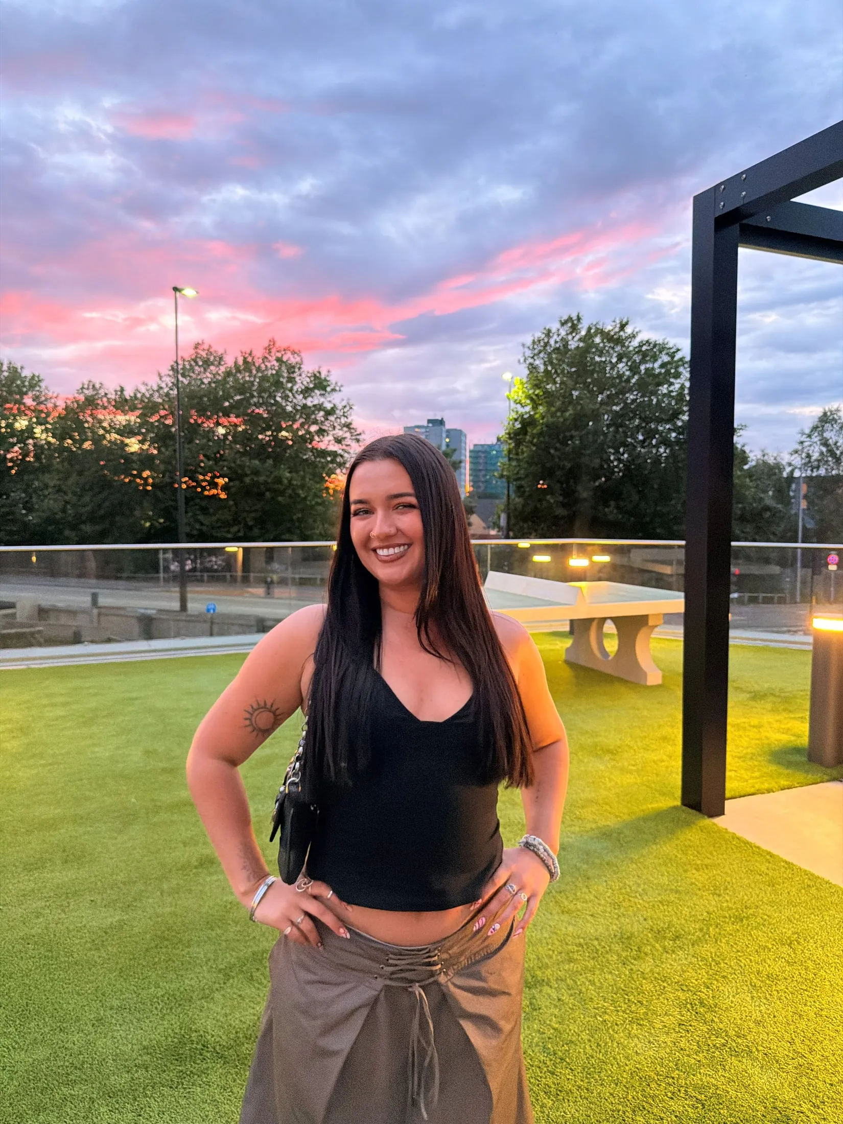 Megan standing on a lawn under a pink evening sky