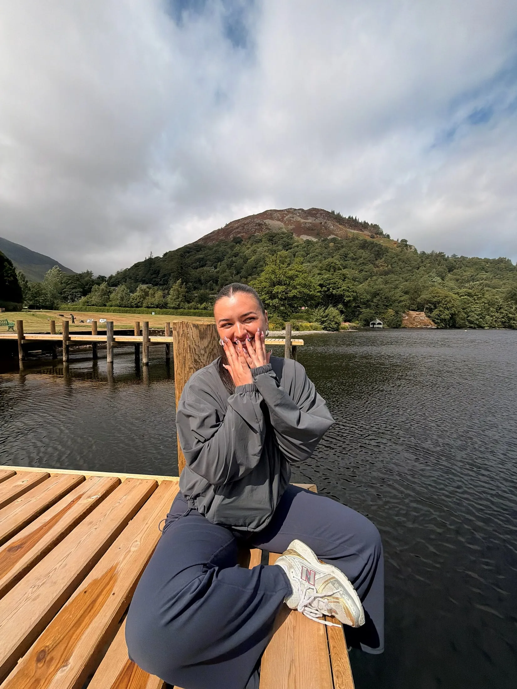 Megan laughing on a wooden jetty by a lake, hands up to her face