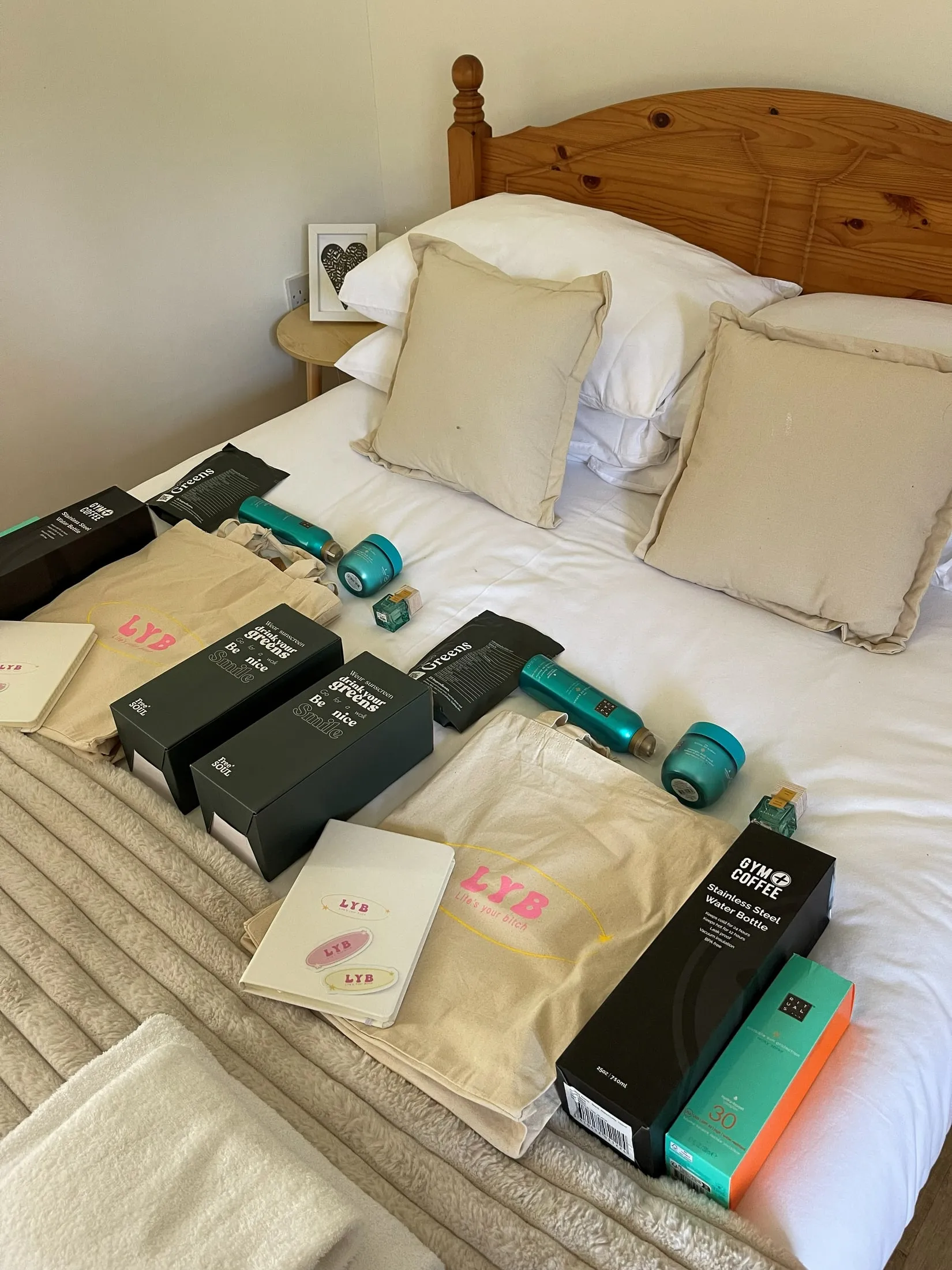 LYB tote bags, notebooks and gifts laid out on a double bed with cream cushions