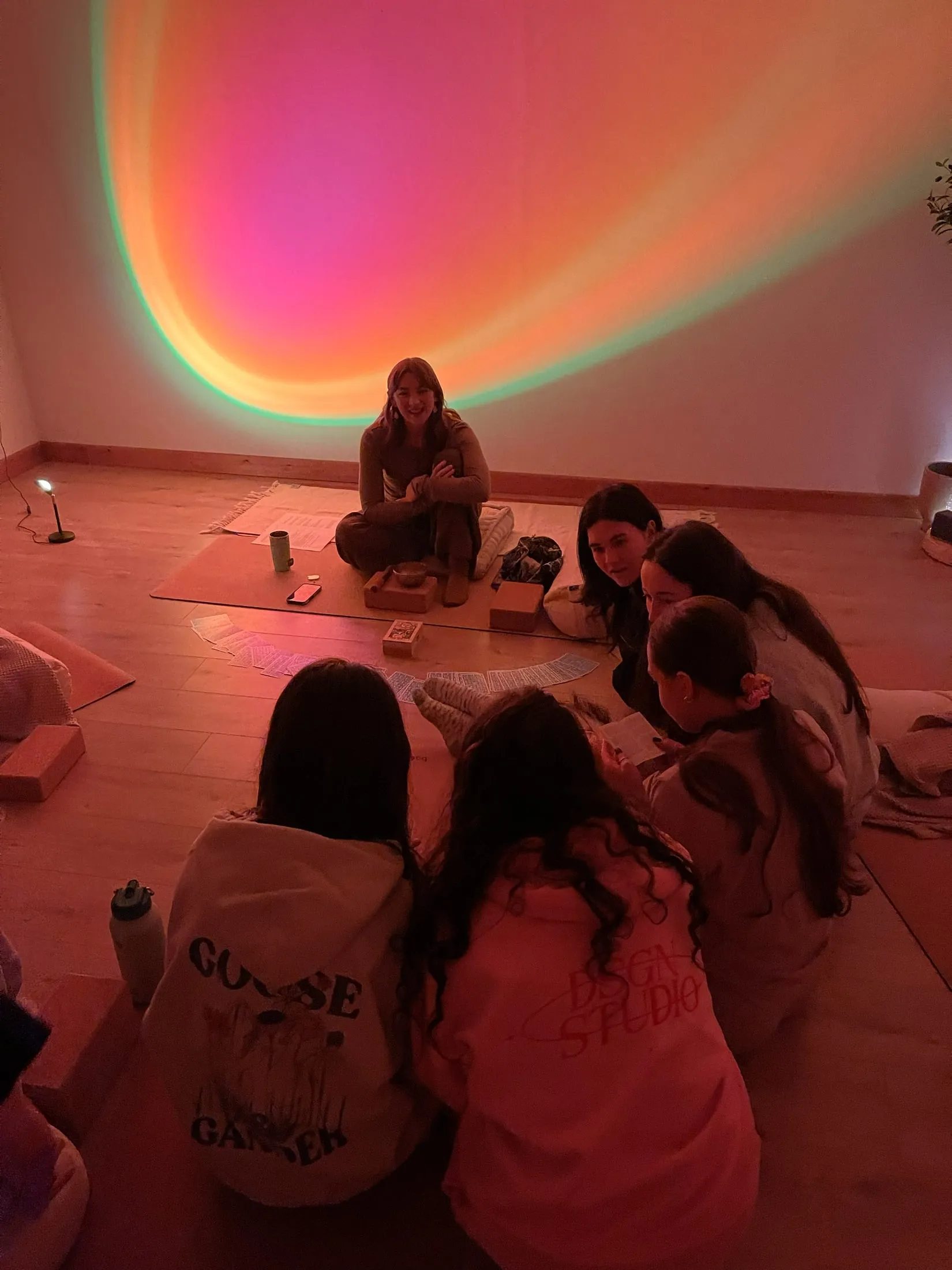 Women sitting on a studio floor, lit pink and orange by a sunset lamp