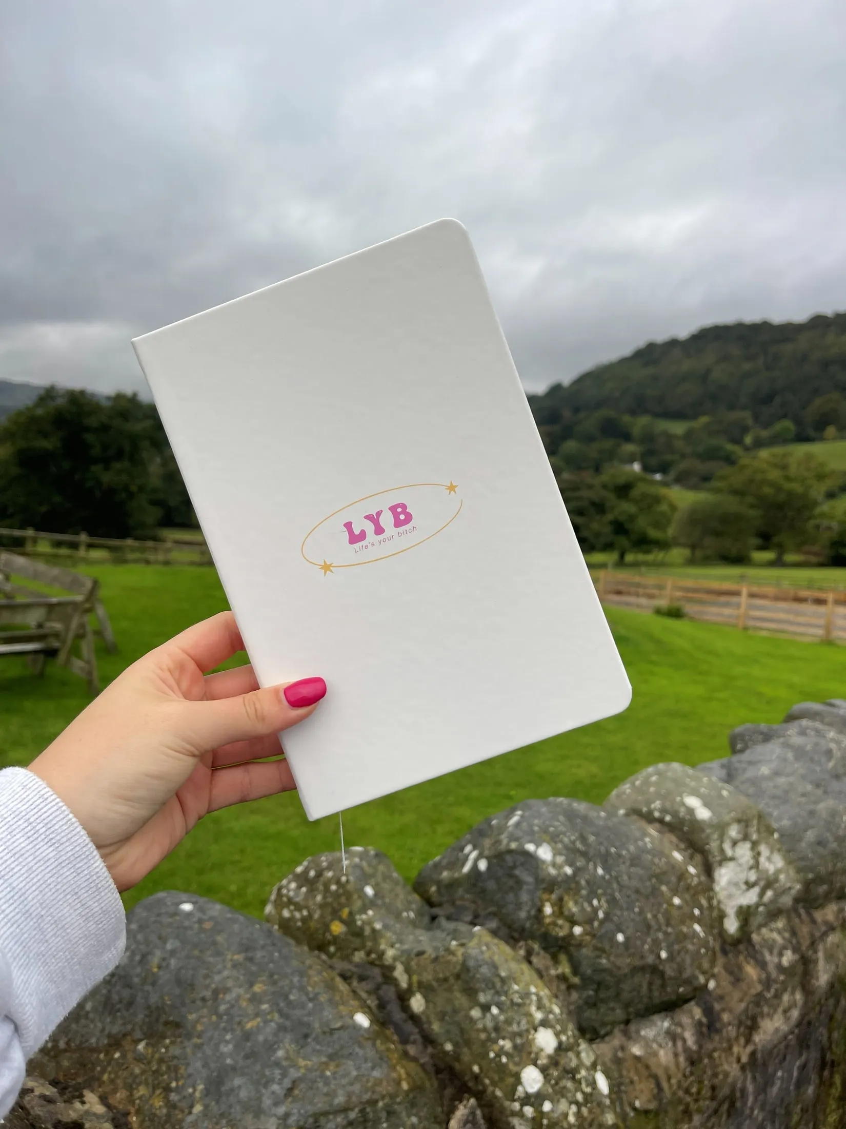 An LYB notebook held up against green hills