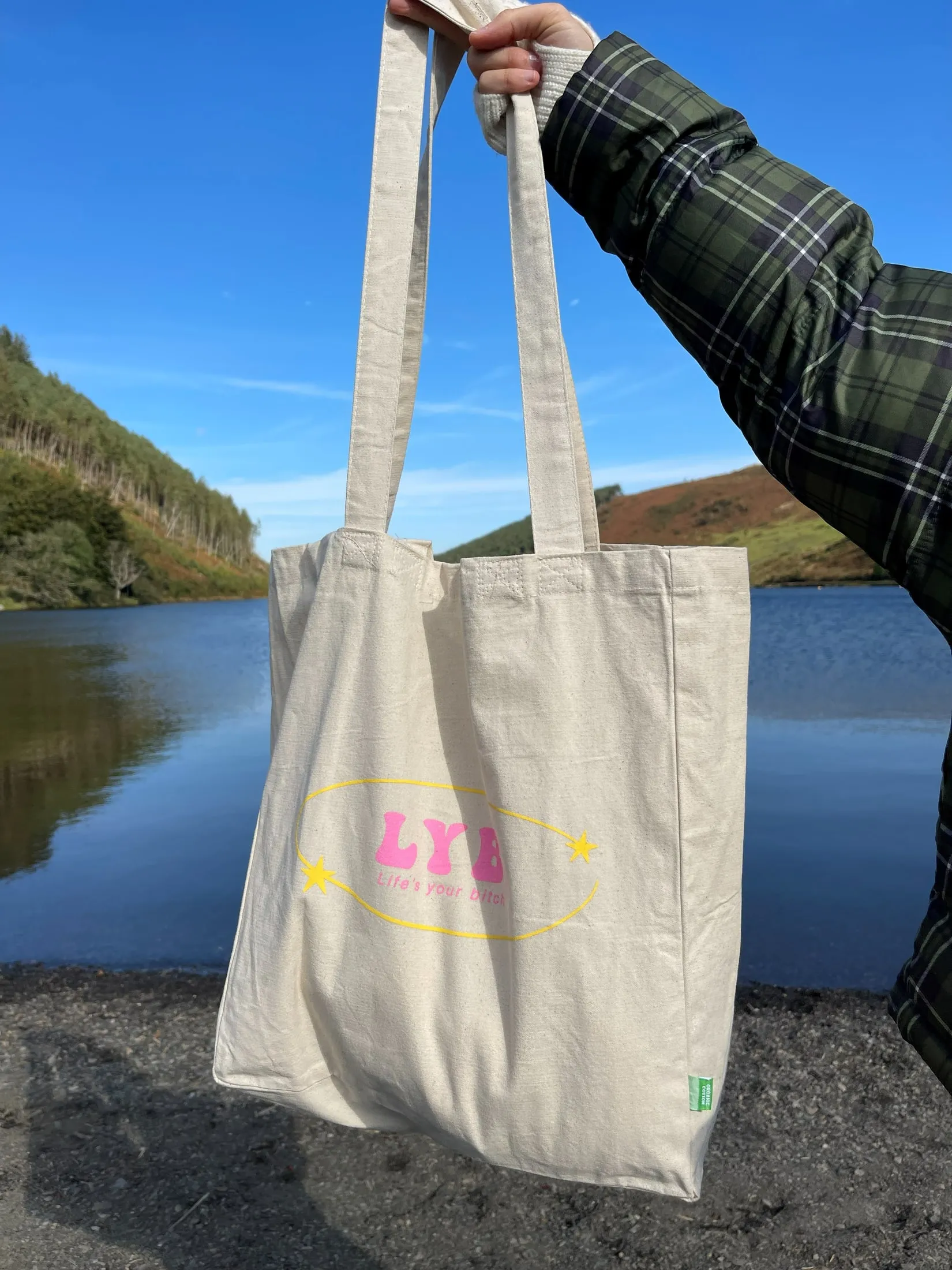 An LYB tote bag held up in front of a lake